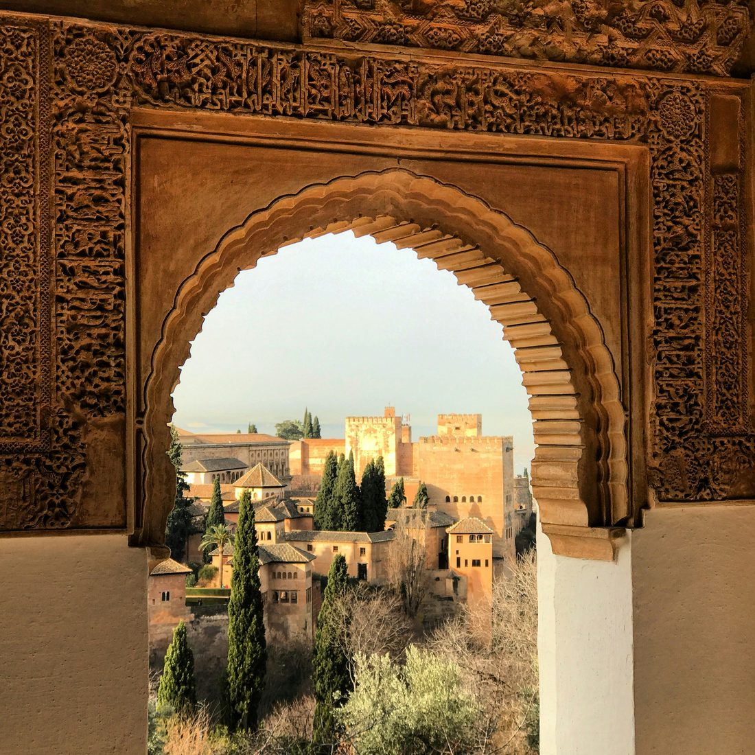 The Alhambra and its Alcazaba towers seen through a carved Nasrid arch from the Generalife, Granada